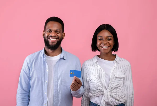 Portrait de heureux couple millénariste noir promouvant les services bancaires, montrant carte de crédit sur fond de studio rose — Photo