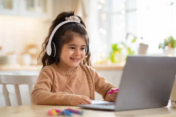 Educación en línea. Linda niña estudio en casa con ordenador portátil y auriculares — Foto de Stock