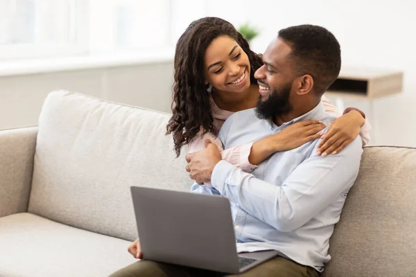 Feliz casal afro-americano amoroso sentado no sofá, usando laptop — Fotografia de Stock