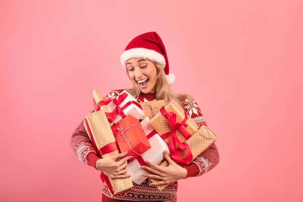 Señora feliz en suéter acogedor y sombrero de Santa celebración montón de regalos sobre fondo rosa. Año Nuevo o celebración de Navidad — Foto de Stock