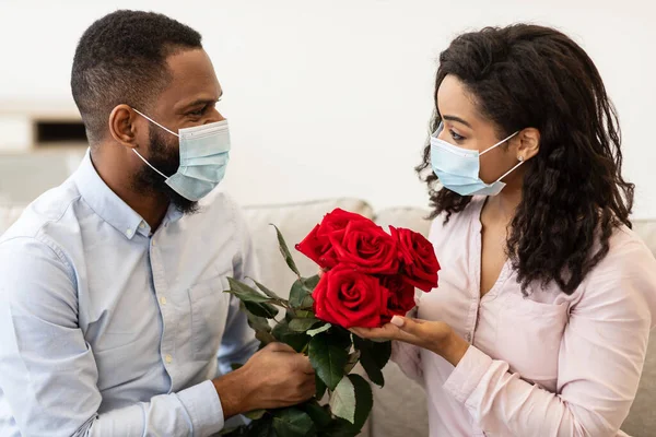 Pareja negra en máscaras médicas teniendo cita, sosteniendo rosas —  Fotos de Stock