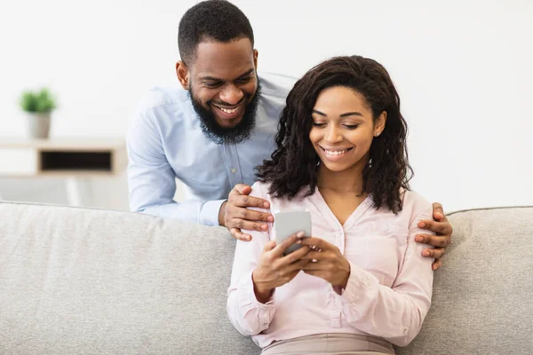 Couple afro-américain assis sur le canapé, en utilisant un téléphone mobile — Photo