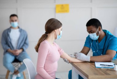 Afrikalı Amerikalı doktor klinikteki genç bayana kovid 19 aşısı enjekte ediyor. Küresel virüse karşı bağışıklık