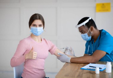Milenyum bayanı koronavirüs aşısı yaptırıyor, baş parmağını kaldırıyor, klinikte koromavirüs aşılanmasını onaylıyor.