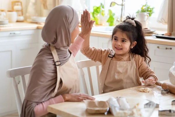 Cheerful มุสลิม แม่ และ ลูกสาว giving high-five ไปยัง แต่ละ อื่น ๆ ใน ห้องครัว — ภาพถ่ายสต็อก