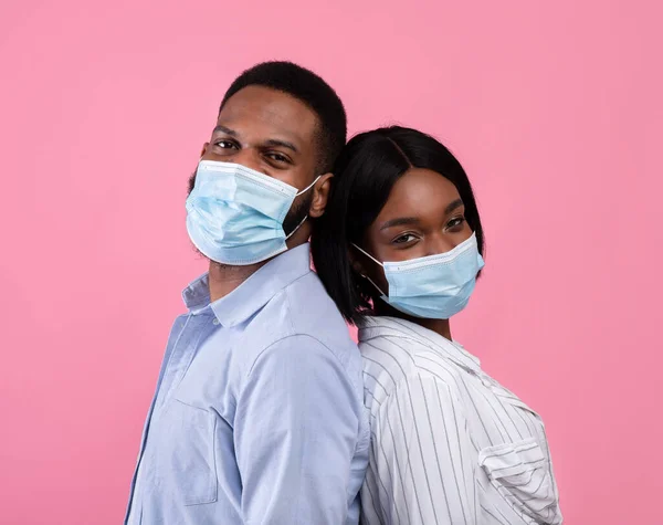 Dia dos Namorados durante a pandemia do covid-19. casal preto usando máscaras faciais, de pé de volta para trás no fundo rosa — Fotografia de Stock