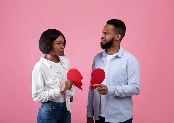 Niezadowolony czarny facet i kobieta trzymający połówki rozdartego serca na różowym tle studia. Pojęcie rozwodu lub zerwania — Zdjęcie stockowe