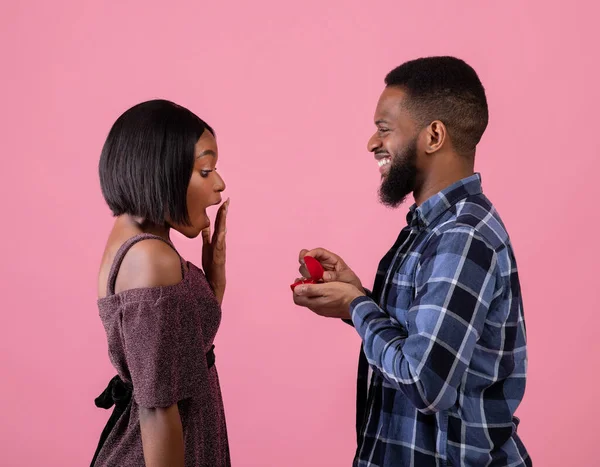 Czarny mężczyzna oświadcza się swojej dziewczynie z diamentowym pierścionkiem na różowym tle studia. Walentynki — Zdjęcie stockowe