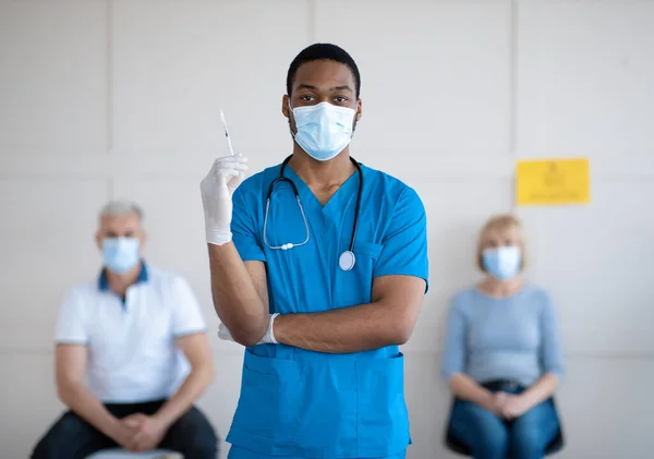 Портрет молодого афроамериканського лікаря в масці і уніфікований шприц з вакциною від коїда-19 в центрі здоров'я — стокове фото