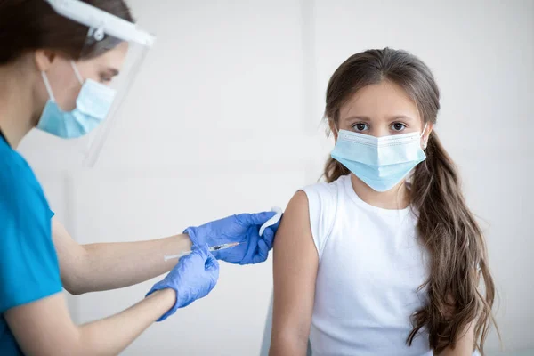 Campaña de inmunización Covid-19. Pequeño paciente con máscara facial que recibe la vacuna contra el coronavirus inyectada por la enfermera en la clínica — Foto de Stock