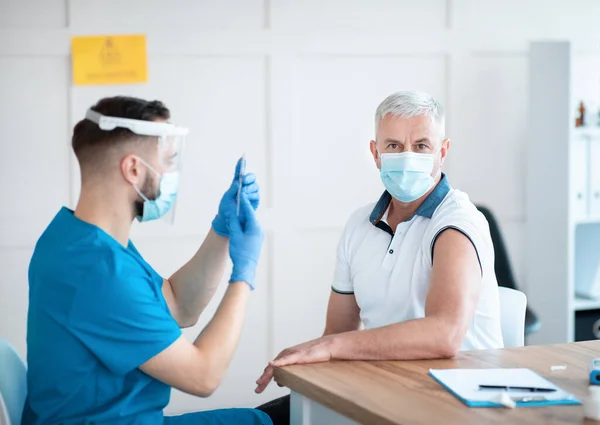 Senior immunizations concept. Young doctor making coronavirus vaccine shot to mature man at medical office — Stock Photo, Image