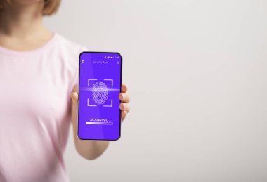 Gri arkaplanda parmak izi tarayıcısı olan telefonu gösteren kadın.