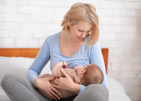 Madre rubia amamantando pequeño bebé, dormitorio interior —  Fotos de Stock
