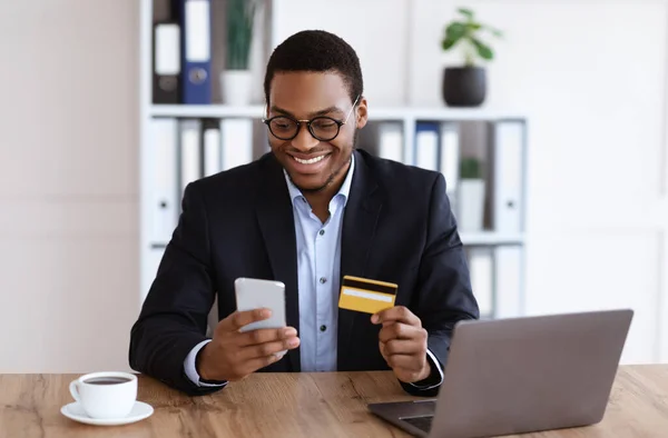 Alegre hombre negro en traje con tarjeta de crédito y teléfono inteligente — Foto de Stock