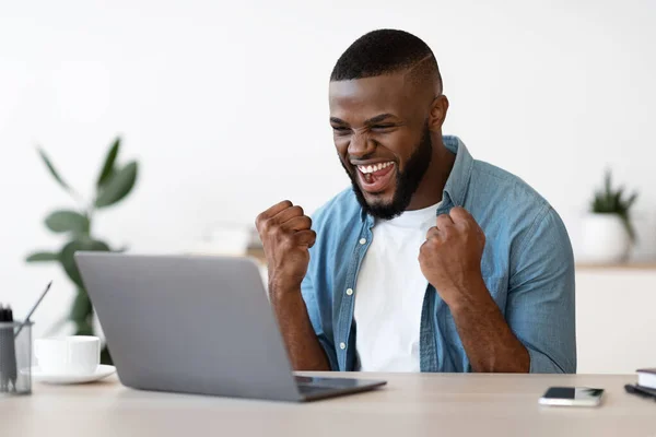 Joyeux homme noir avec ordinateur portable levant les poings sur le lieu de travail, célébrer le succès des entreprises — Photo