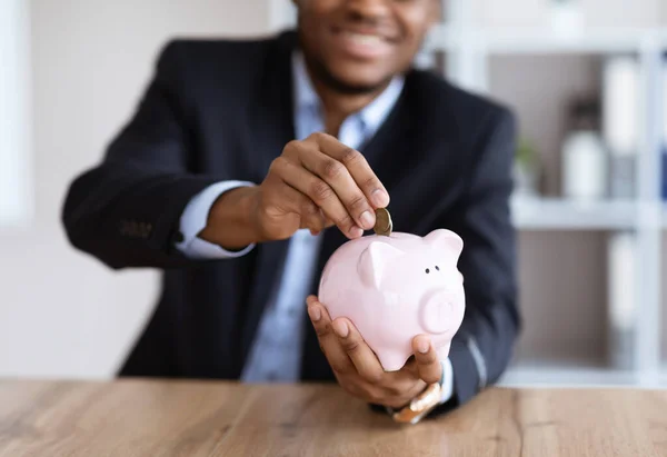 Cultivado de homem de negócios preto colocando dinheiro no banco porquinho — Fotografia de Stock