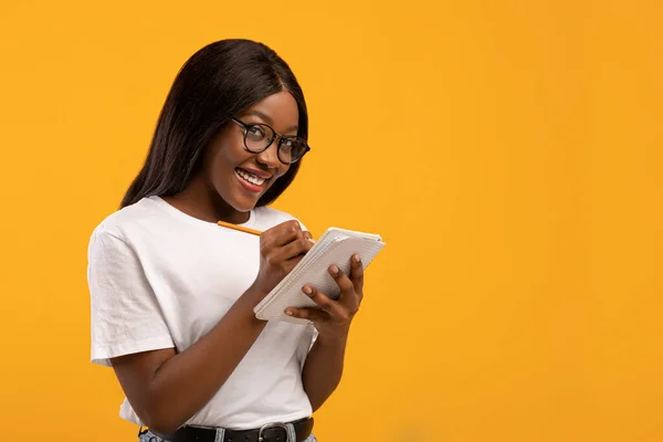 Розумна чорна жінка в окулярах робить нотатки на жовтому — стокове фото