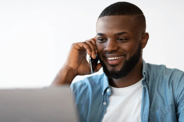 Primer plano retrato de sonriente hombre negro hablando en el teléfono celular y el uso de ordenador portátil —  Fotos de Stock