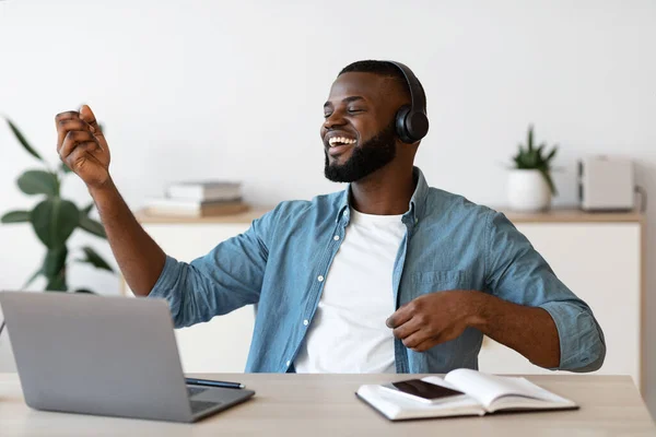 Χαρούμενος μαύρος ελεύθερος άνθρωπος ακούει μουσική και παίζει εικονική κιθάρα στο χώρο εργασίας — Φωτογραφία Αρχείου