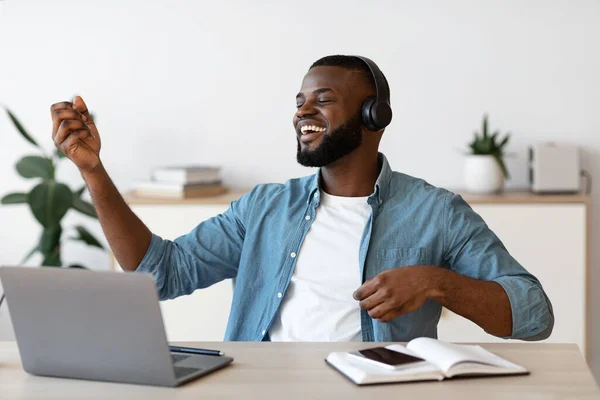 Vrolijke zwarte freelancer man die muziek luistert en virtueel gitaar speelt op het werk — Stockfoto