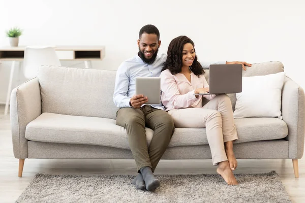 Afrikanisches Paar sitzt auf Couch und benutzt Laptop und Tablet — Stockfoto