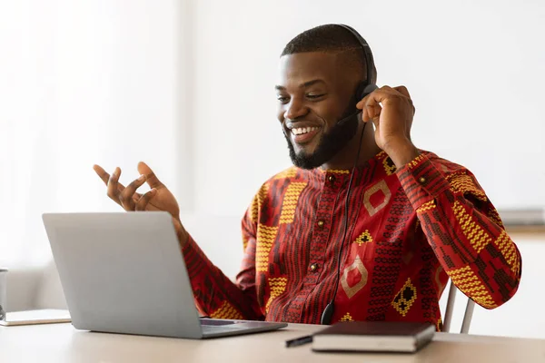 Černošky muž v africké košili dělat video hovor s notebookem a sluchátka — Stock fotografie
