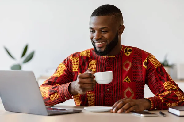 Cheerful African Freelancer Guy Using Laptop And Drinking Morning Coffee At Home — Stock Photo, Image