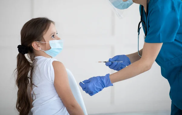 Niña con máscara antiviral que recibe la vacuna covid-19 inyectada por una doctora en el centro de salud — Foto de Stock