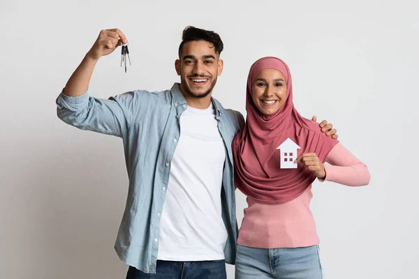 Новый дом. Мусульманская пара держит бумажный дом и ключи на сером фоне — стоковое фото