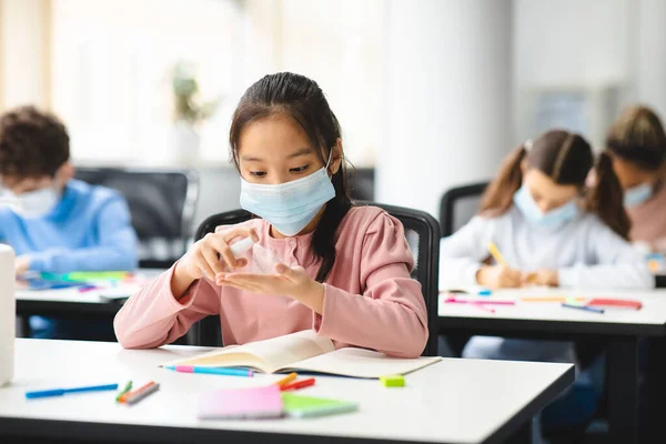 Kis ázsiai diák, aki antibakteriális fertőtlenítőt alkalmaz a kezén — Stock Fotó