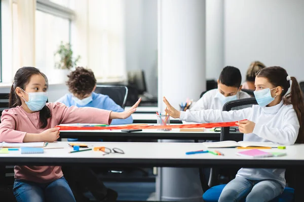 Diverse pupils wearing face masks keeping distance at arms length