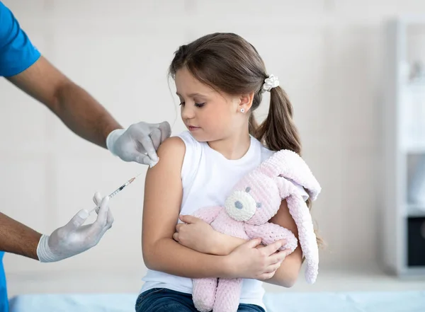 Médecin qui injecte le vaccin contre le coronavirus à une petite fille avec un lapin jouet à la clinique. Médecine et vaccination — Photo