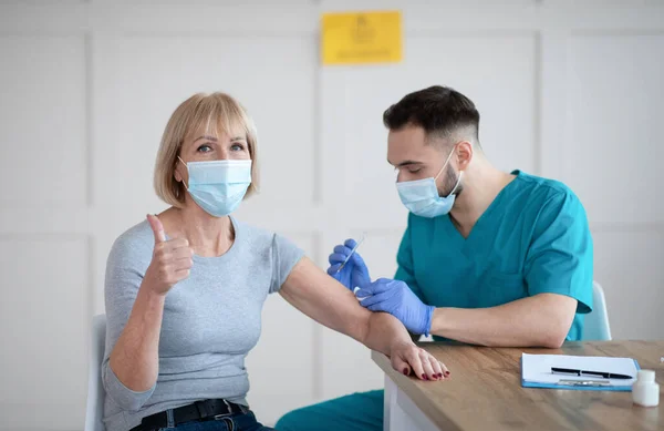 Idős nőbetegek, akik a kovid-19 oltást javasolják, hüvelykujjal mutogatva a coronavirus vakcina beadása alatt — Stock Fotó