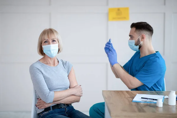 Idős nő, aki a covid-19 injekcióra vár, és fiatal férfi orvos a coronavirus vakcinával az egészségügyi központban — Stock Fotó