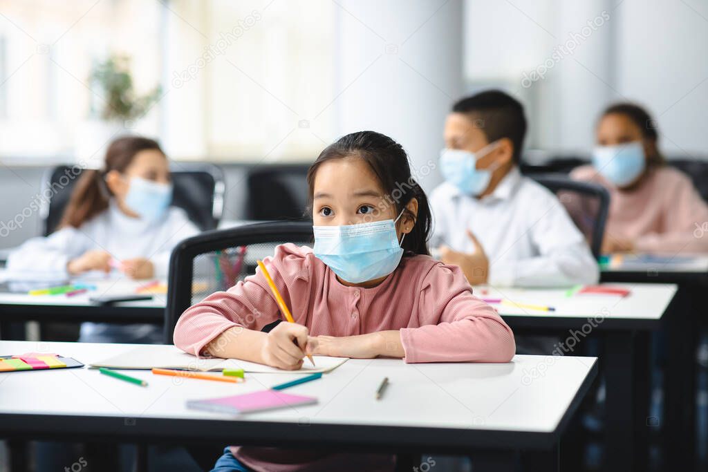 Asian girl in mask sitting at desk in classroom