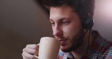 Evde bilgisayarla uğraşırken kulaklık takan, kahve içen genç serbest çalışan ya da oyuncu portresini kapat.