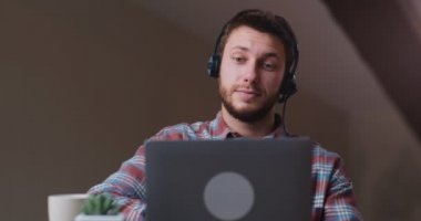 Kulaklıklı genç adam internetten web sitesini izliyor ya da bilgisayarda buluşuyor, ilgili ve odaklanmış görünüyor.