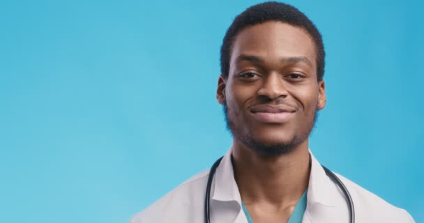 Close-up portret van gelukkig zwart arts houden fan van geld en glimlachen naar camera, blauwe studio achtergrond — Stockvideo
