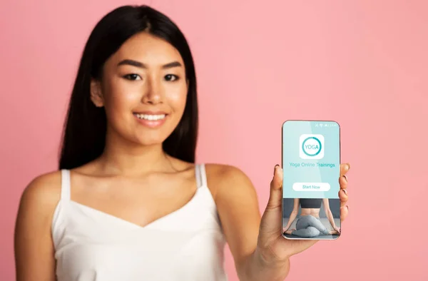 オンラインヨガアプリケーションで電話を示すアジアの女性,ピンクの背景 — ストック写真