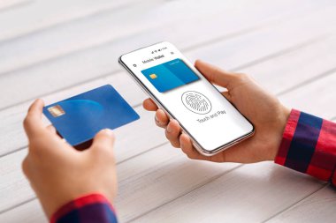 Telefonunu ve kredi kartını kullanan adam ev içinde cüzdanla ödeme yapıyor.