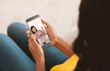 Genç siyahi kadın akıllı telefondan popüler güzellik blogcusunun cilt ürünlerinin video incelemesini izliyor.