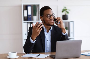 Gülümseyen Afrikalı Amerikalı girişimci ofiste telefonla konuşuyor.