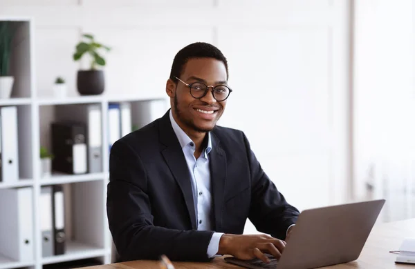 Alegre empresario africano que trabaja con el ordenador portátil en la oficina —  Fotos de Stock