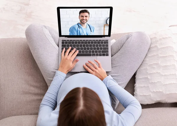 Remote medicine. Top view of pregnant woman getting medical help on internet, consulting doctor on laptop from home