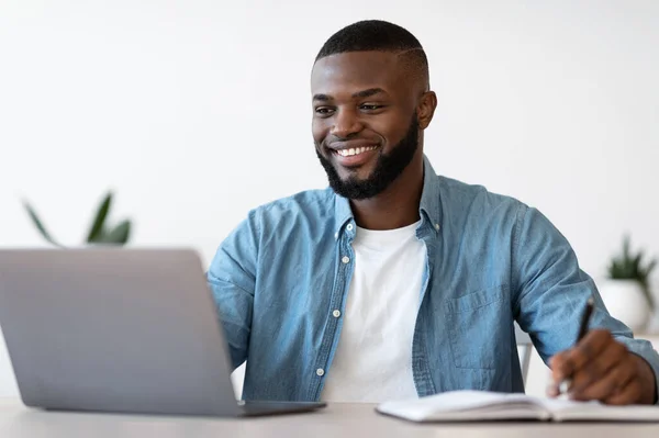 Negro Millennial empresario masculino tomando notas mientras trabaja en el ordenador portátil en la oficina — Foto de Stock