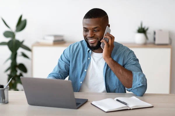 Negocio remoto. Freelancer masculino negro que trabaja con el teléfono celular y el ordenador portátil en casa — Foto de Stock