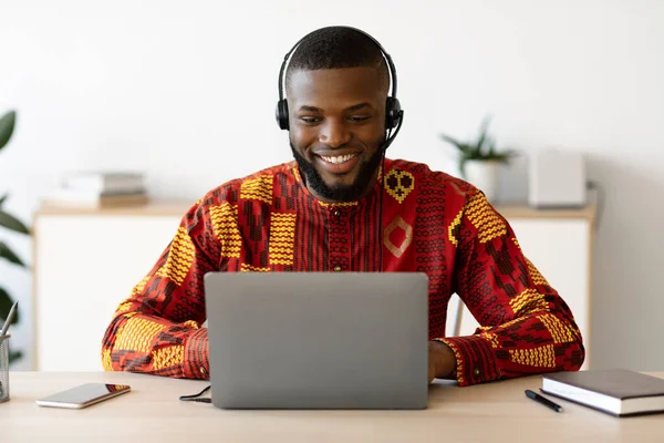 Onderwijs op afstand. zwarte man in Afrikaanse shirt en headset kijken Webinar op laptop — Stockfoto