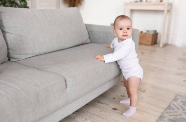 Sevimli küçük bebek kameraya bakıyor. Oturma odasının yanında duruyor.