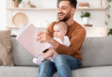 Genç baba evde oturan küçük bebek için kitap okuyor.