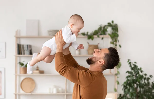 Padre jugando con bebé sosteniendo niño por encima de la cabeza en casa —  Fotos de Stock